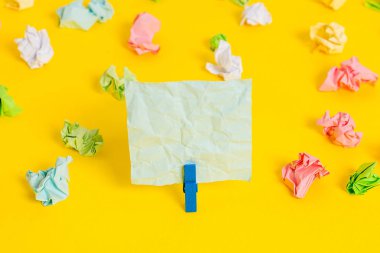Sarı arkaplandaki boş dikdörtgen kare şekilli hatırlatma notunun etrafına yerleştirilmiş renkli buruşuk çarşaflar. Ofis malzemeleri, boş kağıtlar..