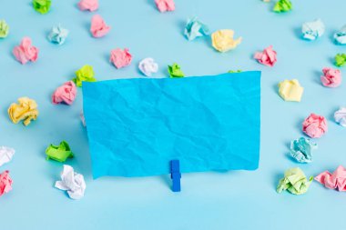 Mavi arka planda boş dikdörtgen kare şeklinde hatırlatma notu etrafında yerleştirilen renkli buruşuk levhalar. Ofis malzemeleri, bir bağlantı elemanı tarafından sabitlenmiş boş kağıt.