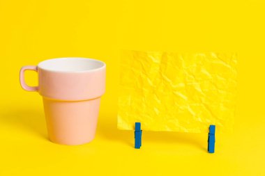 Somon bardağı ve mavi bir çamaşır iğnesi içinde boş bir not kağıdı. Kare dikdörtgen şeklinde renkli anımsatıcı sarı bir arka plan. Boş alan ve ofis malzemeleri.