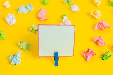 Sarı arkaplandaki boş dikdörtgen kare şekilli hatırlatma notunun etrafına yerleştirilmiş renkli buruşuk çarşaflar. Ofis malzemeleri, boş kağıtlar..