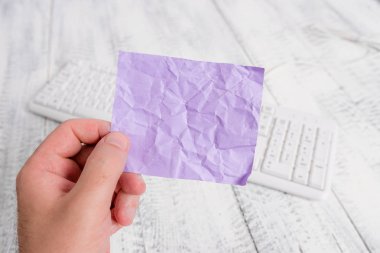 Boş dikdörtgen şeklinde kağıt nota, arka planda beyaz klavye ve hafif ahşap zemin tutan adam. Eller temiz bir arka planda renkli bir hatırlatma alıyor. Boşluk.