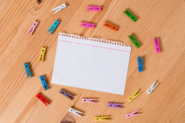 Gekleurde wasknijper verspreid in cirkels rond een lege rechthoek vierkant vormige herinnering notitie in het midden van een houten vloer. Hout met groeven en sleuven. Kantoorbenodigdheden. — Stockfoto