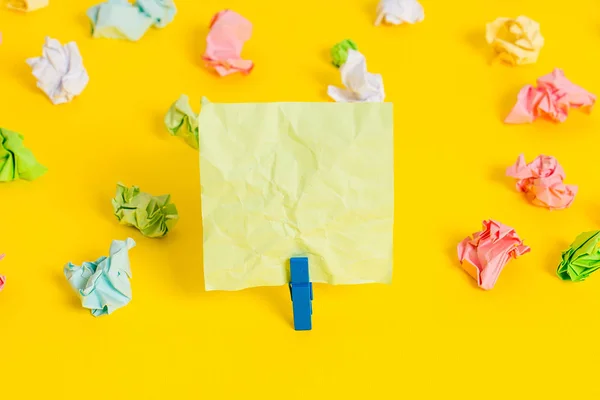 Hojas arrugadas de color colocadas alrededor del rectángulo vacío en forma cuadrada nota recordatorio en el fondo amarillo. Material de oficina, papel en blanco fijado por un cierre. — Foto de Stock