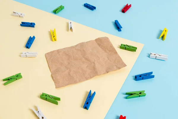 Gekleurde wasknijper geplaatst rond de lege rechthoek vormige herinnering notitie in het midden van een blauwe achtergrond en geel vierkant. Kantoorbenodigdheden, blanco papier vastgemaakt door een bevestiger. — Stockfoto