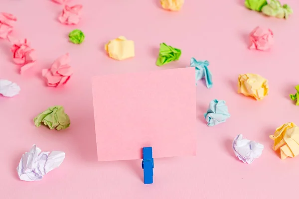 Hojas arrugadas de color colocadas alrededor del rectángulo vacío en forma cuadrada nota recordatorio en el fondo rosa. Material de oficina, papel en blanco fijado por un cierre . — Foto de Stock