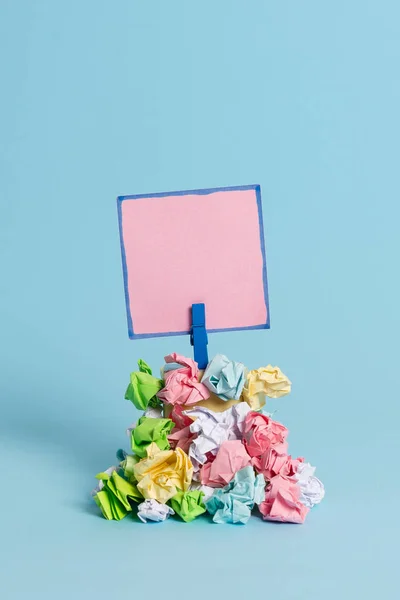Lembrete em forma quadrada acima de uma pilha de papéis amassados fixados por um pano azul. Diferentes folhas empilhadas sob uma nota colorida vazia. Luz azul fundo . — Fotografia de Stock