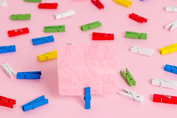 Farbige Wäscheklammer um das leere rechteckige quadratische Erinnerungsstück in der Mitte eines rosafarbenen Hintergrundes platziert. Bürobedarf, unbedrucktes Papier, das mit einem Verschluss befestigt ist. — Stockfoto