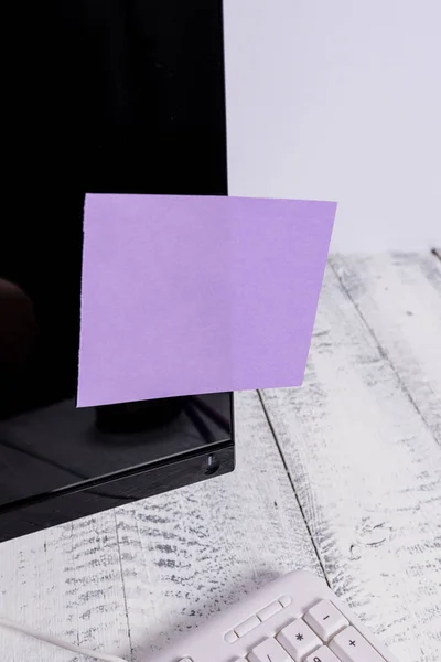表記用紙は、木製のテーブルの上の白いキーボードの近くに黒いコンピュータの画面に貼り付けます。紫色のノートシートがテープで留められたqwertyの近くに置かれたPCモニター. — ストック写真