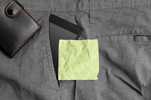 Smartphone készülék a nadrág elülső zsebében egy pénztárca és sárga jegyzet papír. Korszerű szerkentyű van elhelyezett belső rész ember nadrág mellett jelölés lepedő plusz pénztárca — Stock Fotó