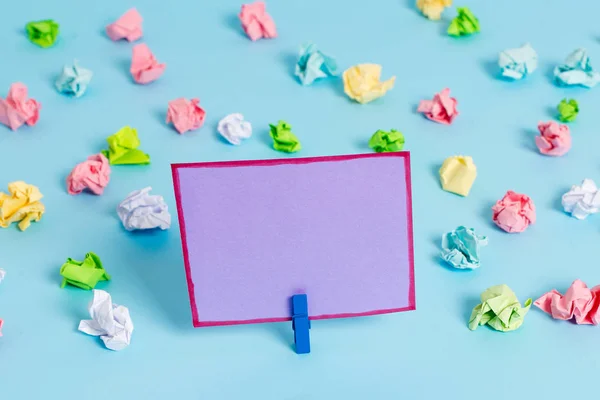 Hojas arrugadas de color colocadas alrededor del rectángulo vacío en forma cuadrada nota recordatorio en el fondo azul. Material de oficina, papel en blanco fijado por un cierre . — Foto de Stock