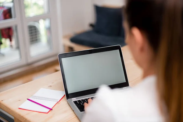 Jonge dame met behulp van een grijze laptop computer en het typen van het zwarte toetsenbord met beide handen in een kamer. Vrouw in een huis ambient met kantoorbenodigdheden en technologische apparaten. — Stockfoto