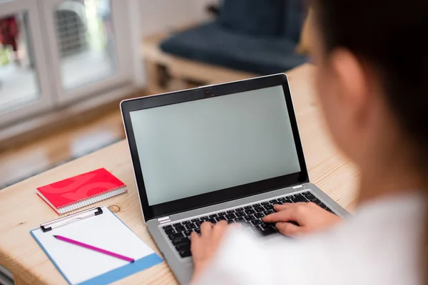 Jonge dame met behulp van een grijze laptop computer en het typen van het zwarte toetsenbord met beide handen in een kamer. Vrouw in een huis ambient met kantoorbenodigdheden en technologische apparaten. — Stockfoto