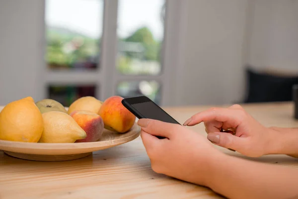 Ung dam med en mörk smartphone i hemmet. Kvinna som håller en svart mobiltelefon i ett hus ambient. Flicka med tekniska enheter och kontorsmateriel med tomt utrymme. — Stockfoto