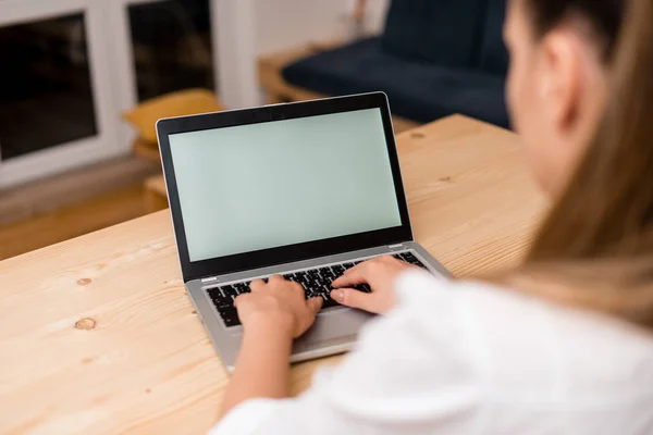 Jonge dame met behulp van een grijze laptop computer en het typen van het zwarte toetsenbord met beide handen in een woonkamer. Kantoorbenodigdheden, technologische apparaten en houten bureau. — Stockfoto