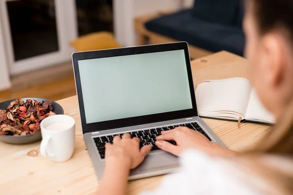 Молодая леди, используя серый ноутбук и печатая на черной клавиатуре с кружкой кофе или чая на заднем плане. Офисные принадлежности, технологические приборы и деревянный стол . — стоковое фото