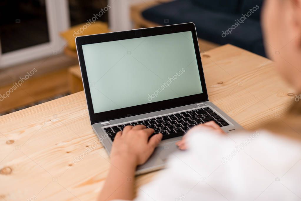 Young lady using a laptop with both hands on the computer. Left hand on the black keyboard and the other on the touchpad. Office supplies, technological devices and wooden desk.