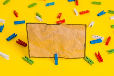 Sarı bir arka plan ortasında boş dikdörtgen kare şeklinde hatırlatma notu etrafında yerleştirilen renkli clothespin. Ofis malzemeleri, bir bağlantı elemanı tarafından sabitlenmiş boş kağıt.