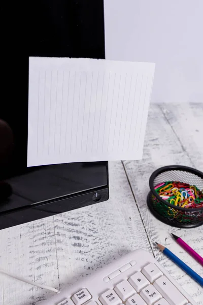 Notatie papier stick naar zwart computerscherm in de buurt van witte toetsenbord en stationair boven de houten tafel. PC-monitor geplaatst in de buurt van schrijf apparatuur met witte notitie blad tape erop. — Stockfoto