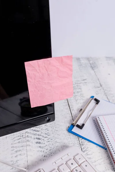 Notatie papier stick naar zwart computerscherm in de buurt van witte toetsenbord en stationair boven de houten tafel. PC-monitor geplaatst in de buurt van schrijf apparatuur met roze notitie blad tape erop. — Stockfoto