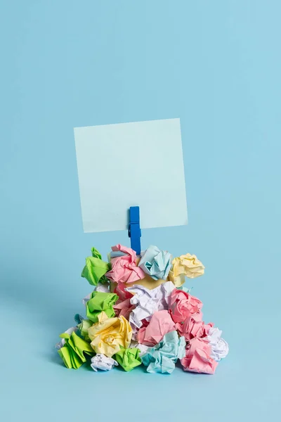 Recordatorio en forma cuadrada sobre una pila de papeles arrugados fijados por un pasador de ropa azul. Diferentes hojas apiladas bajo una nota colorida vacía. Fondo azul claro . —  Fotos de Stock