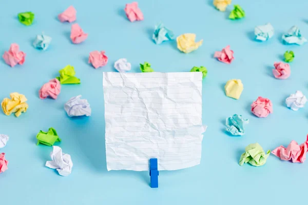 Hojas arrugadas de color colocadas alrededor del rectángulo vacío en forma cuadrada nota recordatorio en el fondo azul. Material de oficina, papel en blanco fijado por un cierre . —  Fotos de Stock