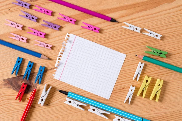 Farbige Wäscheklammer um das leere rechteckige quadratische Erinnerungsstück in der Mitte eines Holzfußbodens platziert. Holz mit Nuten und Schlitzen. Bürobedarf, Bleistift und Stift. — Stockfoto