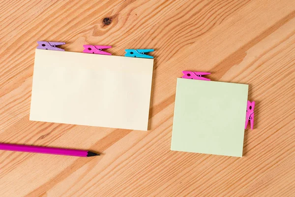 Espina de ropa de color colocada alrededor del rectángulo vacío en forma cuadrada nota recordatorio en el centro de un piso de madera. Madera con ranuras y ranuras. Material de oficina, lápiz y bolígrafo . — Foto de Stock