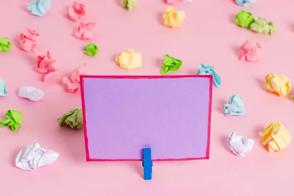 Folhas de crumpled coloridas colocadas em torno da nota de lembrete em forma quadrada retangular vazia no fundo rosa. Material de escritório, papel em branco fixado por um fixador . — Fotografia de Stock