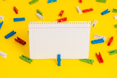 Sarı bir arka plan ortasında boş dikdörtgen kare şeklinde hatırlatma notu etrafında yerleştirilen renkli clothespin. Ofis malzemeleri, bir bağlantı elemanı tarafından sabitlenmiş boş kağıt.