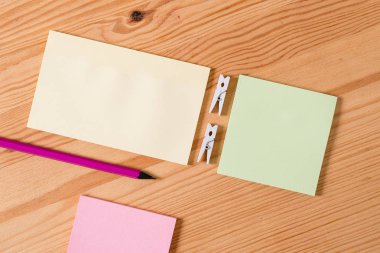 Ahşap bir zeminin ortasında boş dikdörtgen kare şeklinde hatırlatma notu etrafında yerleştirilen renkli clothespin. Oluklar ve yuvaları ile ahşap. Ofis malzemeleri, kalem ve kalem.