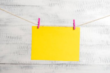 Dikdörtgen şeklinde not renkli kağıt beyaz ahşap arka planda clothespin tarafından bir çamaşır ipi kırpılmış. Kare boş hatırlatma ve ofis ekipmanları malzemeleri hafif ahşap bir masada.