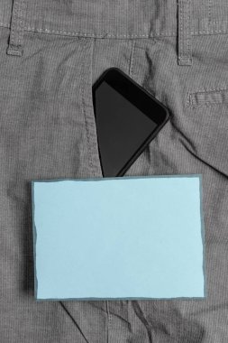 Mavi bir not kağıt yakınında resmi çalışma pantolon ön cebinde siyah akıllı telefon cihazı. Modern gadget notasyon levha yakın erkek pantolon içine yerleştirilir