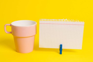 Somon bardağı ve mavi bir çamaşır iğnesi içinde boş bir not kağıdı. Kare dikdörtgen şeklinde renkli anımsatıcı sarı bir arka plan. Boş alan ve ofis malzemeleri.