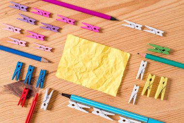 Ahşap bir zeminin ortasında boş dikdörtgen kare şeklinde hatırlatma notu etrafında yerleştirilen renkli clothespin. Oluklar ve yuvaları ile ahşap. Ofis malzemeleri, kalem ve kalem.