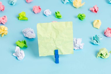 Mavi arka planda boş dikdörtgen kare şeklinde hatırlatma notu etrafında yerleştirilen renkli buruşuk levhalar. Ofis malzemeleri, bir bağlantı elemanı tarafından sabitlenmiş boş kağıt.
