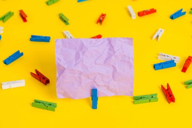 Sarı bir arka plan ortasında boş dikdörtgen kare şeklinde hatırlatma notu etrafında yerleştirilen renkli clothespin. Ofis malzemeleri, bir bağlantı elemanı tarafından sabitlenmiş boş kağıt.