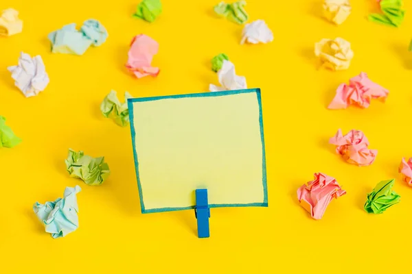 Folhas de crumpled coloridas colocadas em torno da nota de lembrete em forma quadrada retangular vazia no fundo amarelo. Material de escritório, papel em branco fixado por um fixador. — Fotografia de Stock