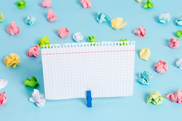 Hojas arrugadas de color colocadas alrededor del rectángulo vacío en forma cuadrada nota recordatorio en el fondo azul. Material de oficina, papel en blanco fijado por un cierre . — Foto de Stock