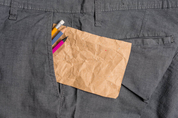Writing equipment and a brown note paper inside the formal working trousers front pocket. Stationary pencil with notation sheet placed in man work pants