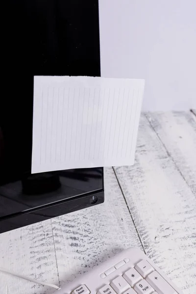 表記用紙は、木製のテーブルの上の白いキーボードの近くに黒いコンピュータの画面に貼り付けます。白いノートシートがテープで留められたqwertyの近くに置かれたPCモニター. — ストック写真