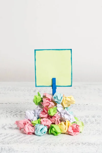 Rappel carré au-dessus d'une pile de papiers froissés fixés par une pince à linge bleue. Différentes feuilles empilées sous une note colorée vide. Sol en bois blanc et fond blanc . — Photo