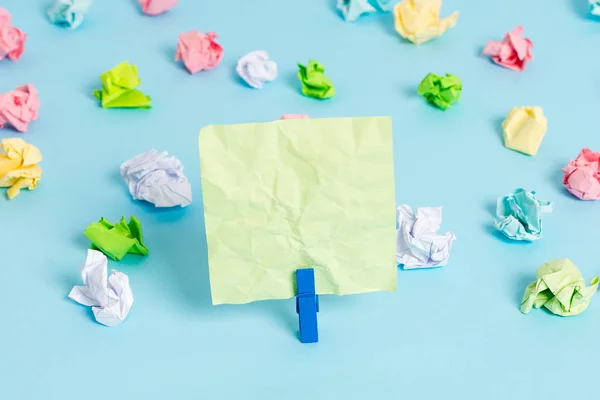 Hojas arrugadas de color colocadas alrededor del rectángulo vacío en forma cuadrada nota recordatorio en el fondo azul. Material de oficina, papel en blanco fijado por un cierre . — Foto de Stock