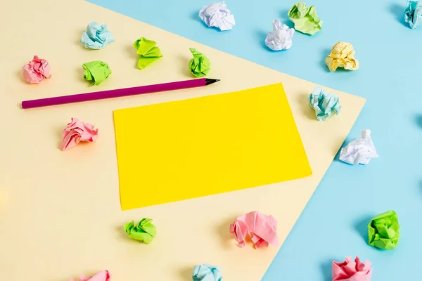 Folhas de crumpled coloridas e um lápis colocado em torno da nota de lembrete em forma de retângulo vazio no centro de um fundo azul e quadrado amarelo. Material de escritório, fixador . — Fotografia de Stock