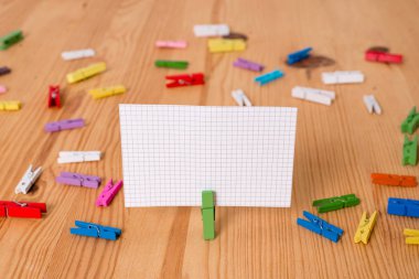 Renkli clothespin ahşap bir zemin ortasında boş bir dikdörtgen kare şeklinde hatırlatma notu etrafında yayıldı. Oluklar ve yuvaları ile ahşap. Ofis malzemeleri.