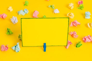 Sarı arkaplandaki boş dikdörtgen kare şekilli hatırlatma notunun etrafına yerleştirilmiş renkli buruşuk çarşaflar. Ofis malzemeleri, boş kağıtlar..