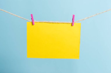 Dikdörtgen şeklinde not renkli kağıt beyaz ahşap arka planda clothespin tarafından bir çamaşır ipi kırpılmış. Kare boş hatırlatma ve ofis ekipmanları malzemeleri hafif ahşap bir masada.