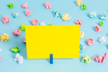 Mavi arka planda boş dikdörtgen kare şeklinde hatırlatma notu etrafında yerleştirilen renkli buruşuk levhalar. Ofis malzemeleri, bir bağlantı elemanı tarafından sabitlenmiş boş kağıt.