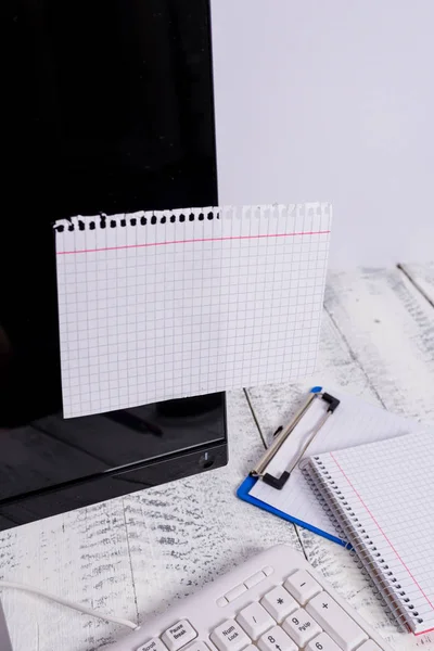 Notatie papier stick naar zwart computerscherm in de buurt van witte toetsenbord en stationair boven de houten tafel. PC-monitor geplaatst in de buurt van schrijf apparatuur met witte notitie blad tape erop. — Stockfoto