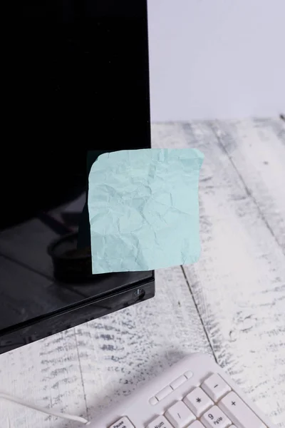 表記用紙は、木製のテーブルの上の白いキーボードの近くに黒いコンピュータの画面に貼り付けます。青いノートシートがテープで留められたqwertyの近くに置かれたPCモニター. — ストック写真