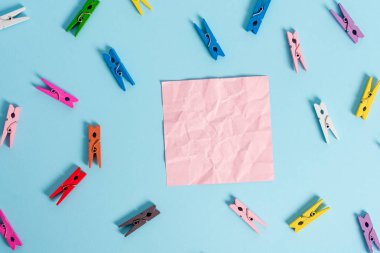 Renkli clothespin açık mavi bir arka plan içinde dikdörtgen kare şeklinde renkli kağıt etrafında yayıldı. Boş bir alana anımsatıcı notu. Bir masada ofis malzemeleri.